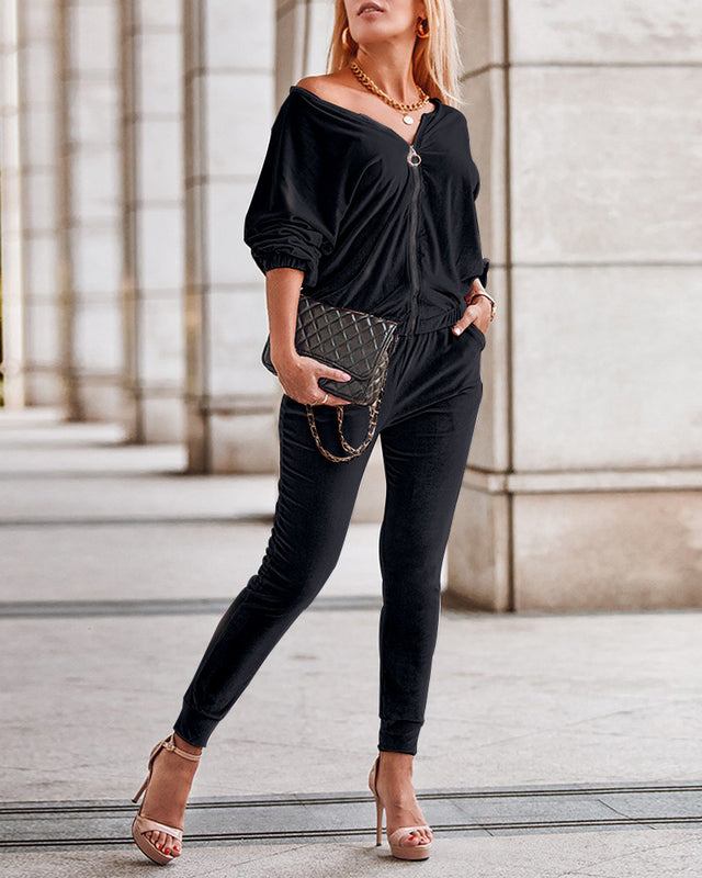 Donna in abito nero elegante, con borsa a tracolla trapuntata e sandali con tacco, posa in un ambiente urbano. Moda femminile chic e sofisticata.