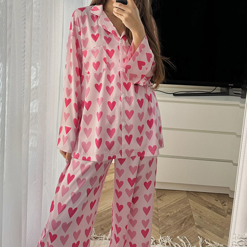 Donna in pigiama rosa con cuori rossi, davanti a un mobile bianco e una TV. Moda notte, abbigliamento comodo, stile romantico.