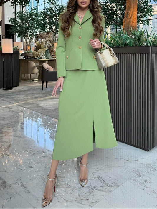Donna in elegante tailleur verde, giacca con bottoni dorati, gonna lunga con spacco. Indossa tacchi scintillanti e borsa dorata. Ambiente lussuoso.