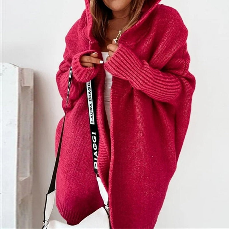 Donna con cardigan oversize rosso, cappuccio e borsa a tracolla bianca. Moda autunnale, abbigliamento casual, stile confortevole.