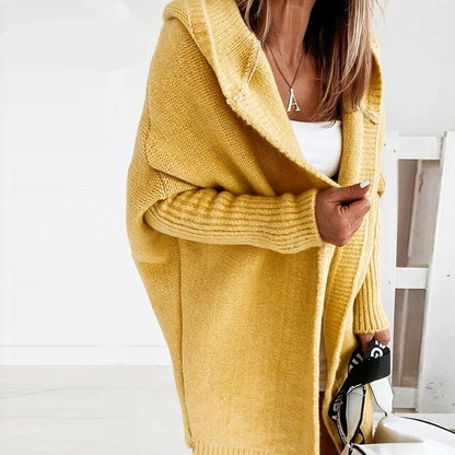 Donna con cardigan giallo oversize, maglia bianca e collana con ciondolo a forma di A. Moda autunnale, abbigliamento casual elegante.