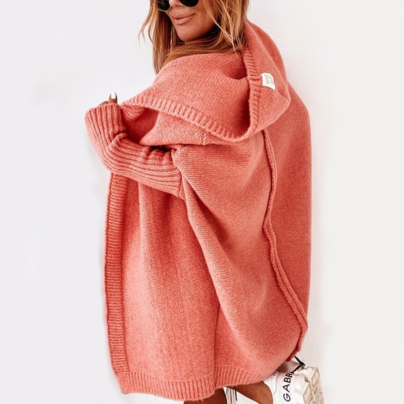 Donna con cardigan oversize rosa, cappuccio ampio, occhiali da sole, scarpe bianche. Moda autunnale, abbigliamento casual elegante.
