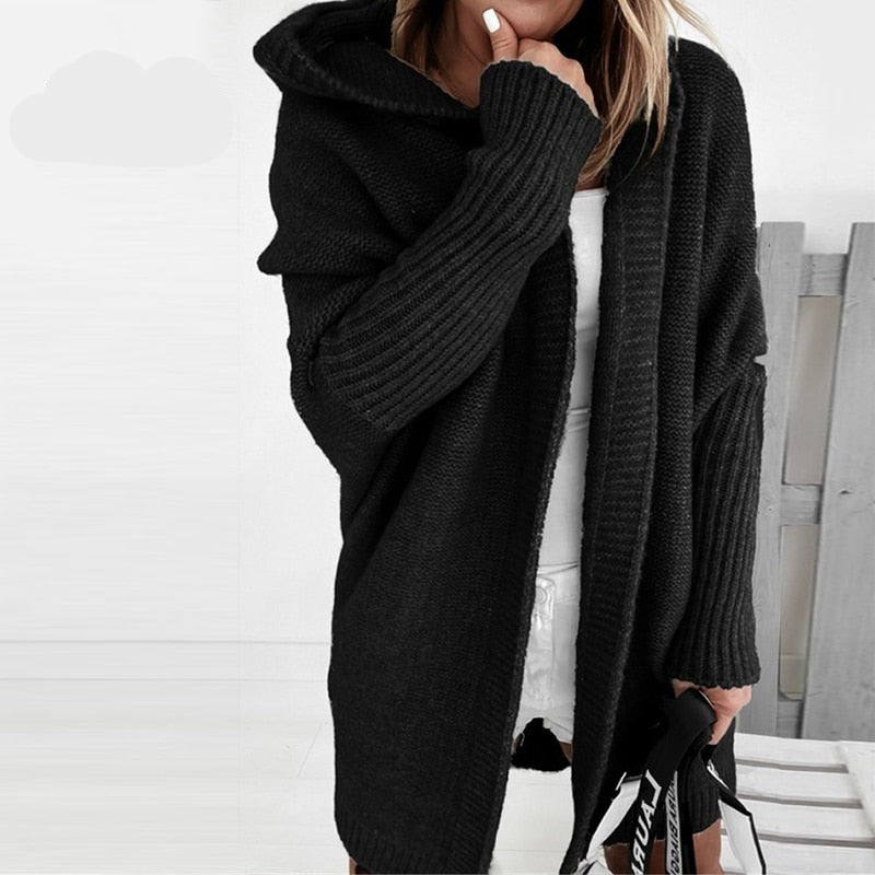 Donna con cardigan nero oversize, cappuccio e maniche lunghe, abbinato a vestito bianco. Moda autunnale, stile casual chic.