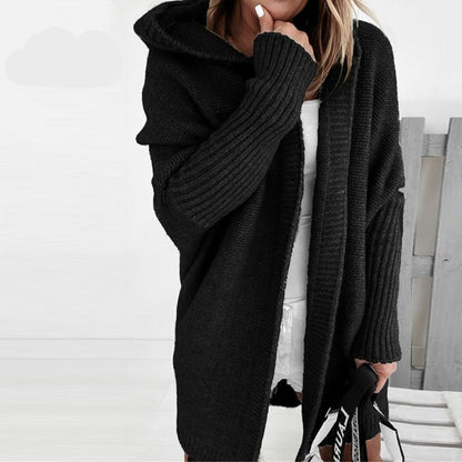 Donna con cardigan nero oversize, cappuccio e maniche lunghe, abbinato a vestito bianco. Moda autunnale, stile casual chic.