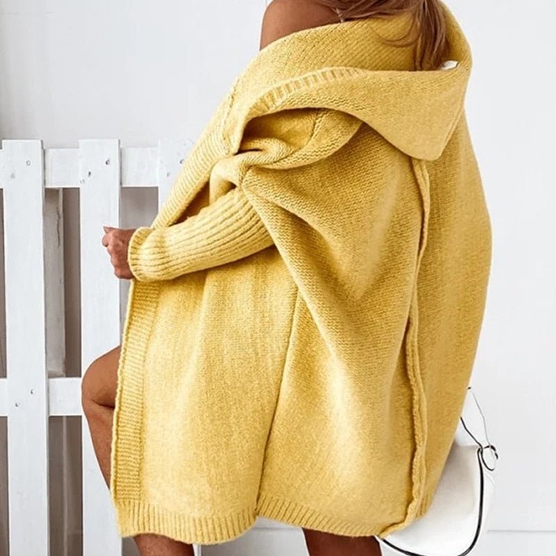 Donna con cardigan oversize giallo, seduta di profilo. Moda autunnale, maglione caldo, stile casual chic. Sfondo bianco minimalista.