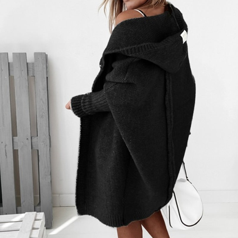 Donna con cappotto nero oversize in maglia, cappuccio, borsa bianca. Moda autunno inverno, abbigliamento casual elegante.