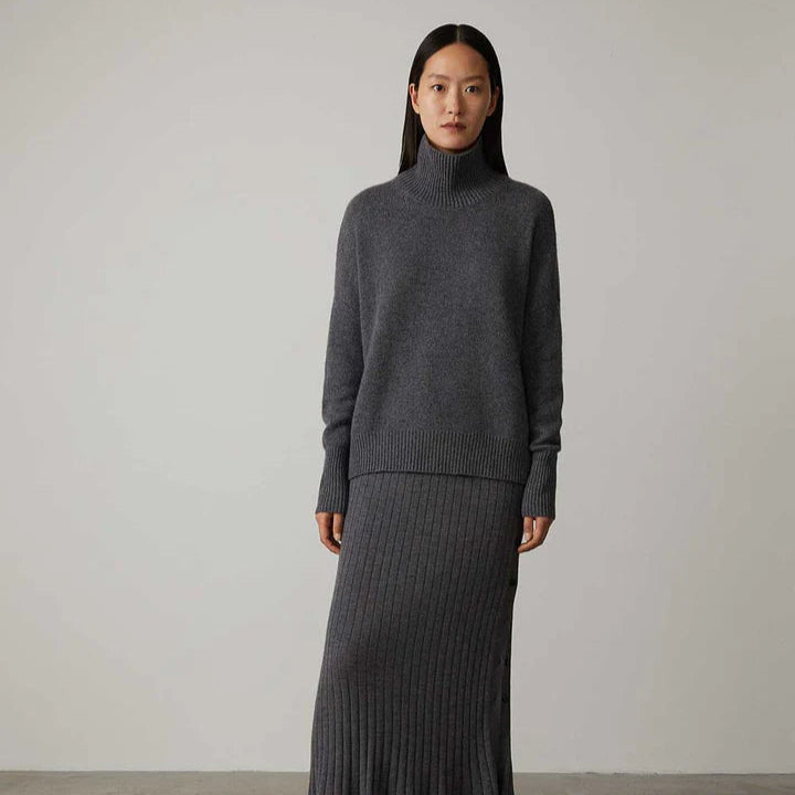 Donna con maglione grigio a collo alto e gonna lunga a coste, moda autunno inverno, abbigliamento casual elegante, sfondo neutro.