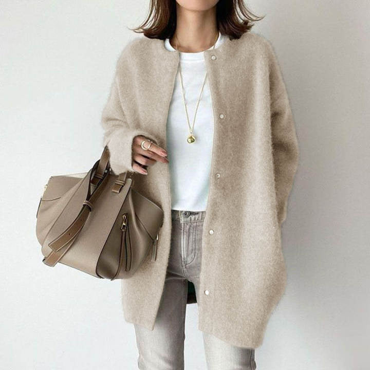 Donna con cardigan beige, borsa a tracolla marrone, jeans chiari e collana dorata. Moda autunnale casual chic. Abbigliamento femminile elegante.