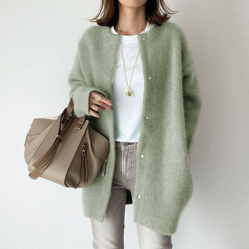 Donna con cardigan verde chiaro, borsa beige e jeans grigi. Moda autunnale, stile casual chic, accessori eleganti.