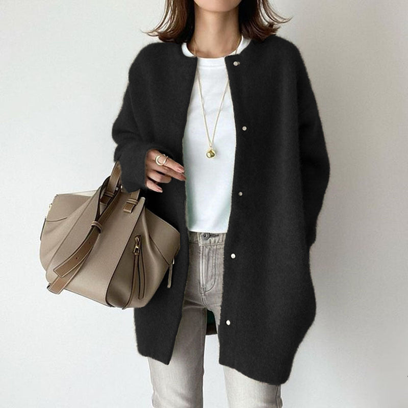 Donna con cardigan nero, borsa beige, jeans grigi e collana dorata. Moda autunnale casual chic, outfit elegante e moderno.