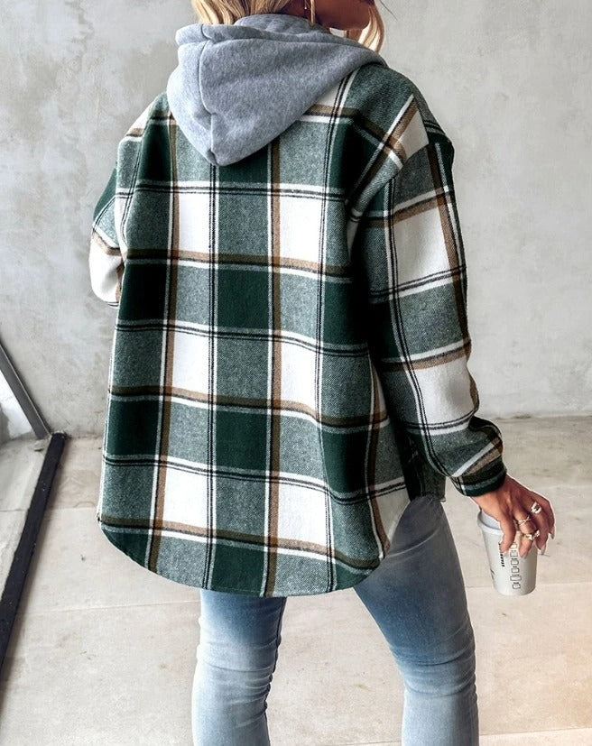 Donna con camicia a quadri verde e bianca, cappuccio grigio, jeans aderenti, tiene una tazza da viaggio. Moda casual autunnale, stile urbano.
