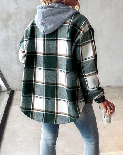 Donna con camicia a quadri verde e bianca, cappuccio grigio, jeans aderenti, tiene una tazza da viaggio. Moda casual autunnale, stile urbano.