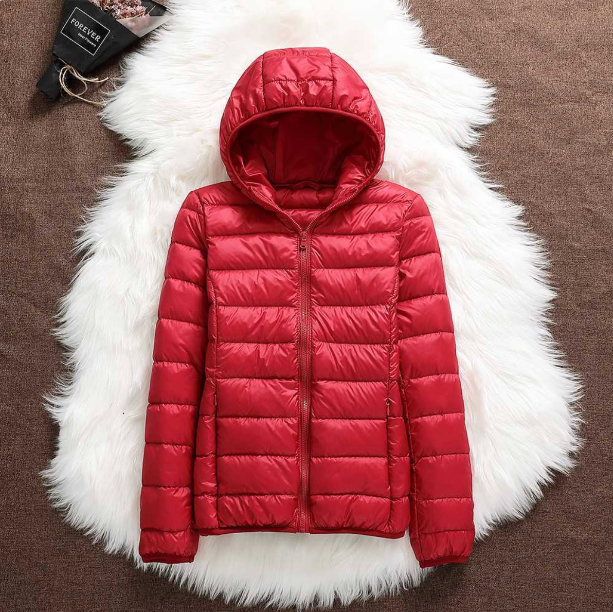 Giacca invernale rossa con cappuccio, imbottita e trapuntata, su sfondo di pelliccia bianca. Moda donna, abbigliamento caldo, stile casual.