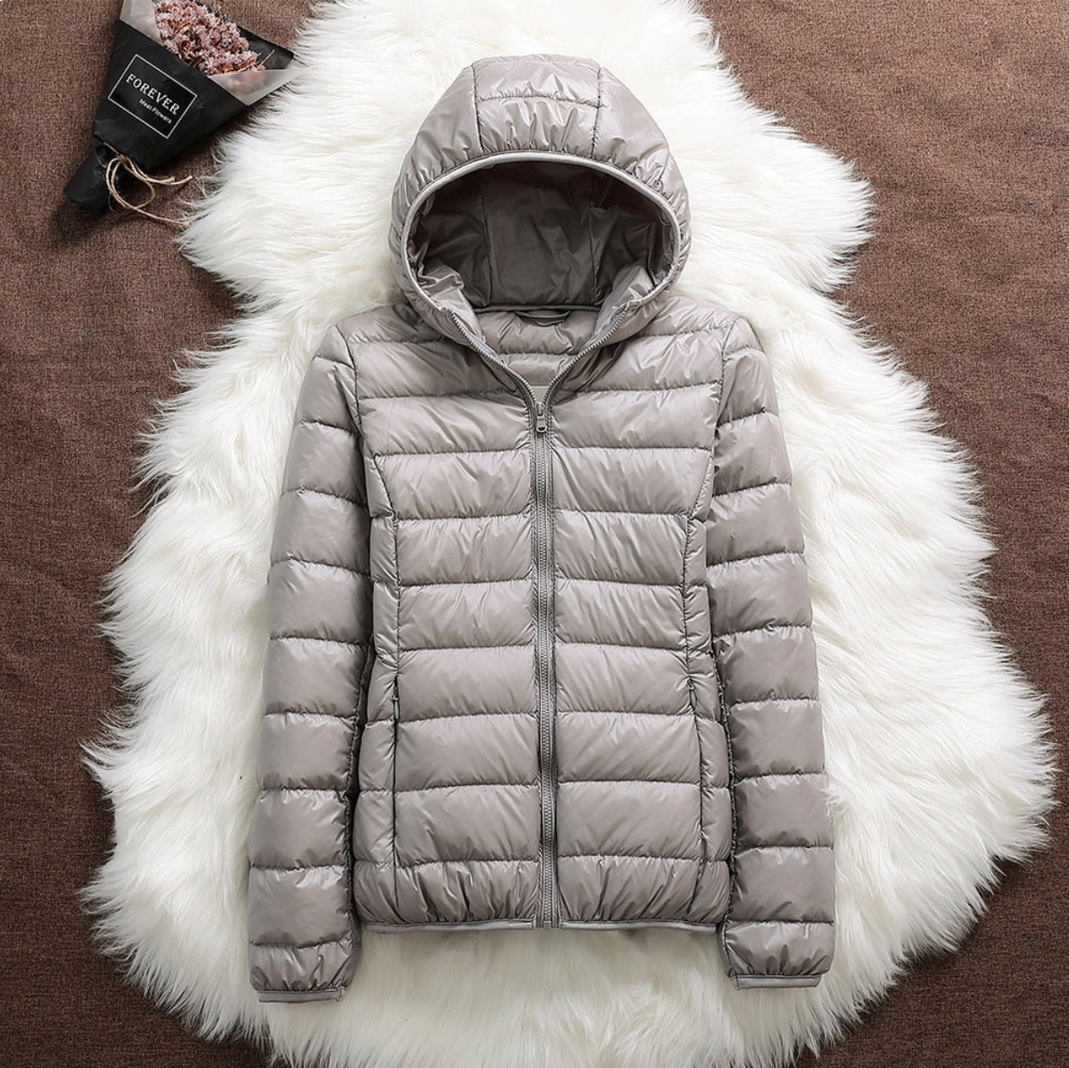 Giacca invernale imbottita grigia con cappuccio su sfondo di pelliccia bianca, moda donna, abbigliamento caldo, stile casual, tendenza autunno inverno.