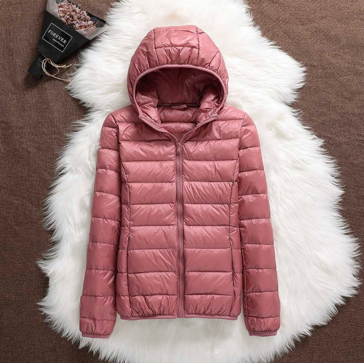 Giacca invernale rosa con cappuccio su sfondo di pelliccia bianca, design trapuntato, moda donna, abbigliamento caldo, stile casual.