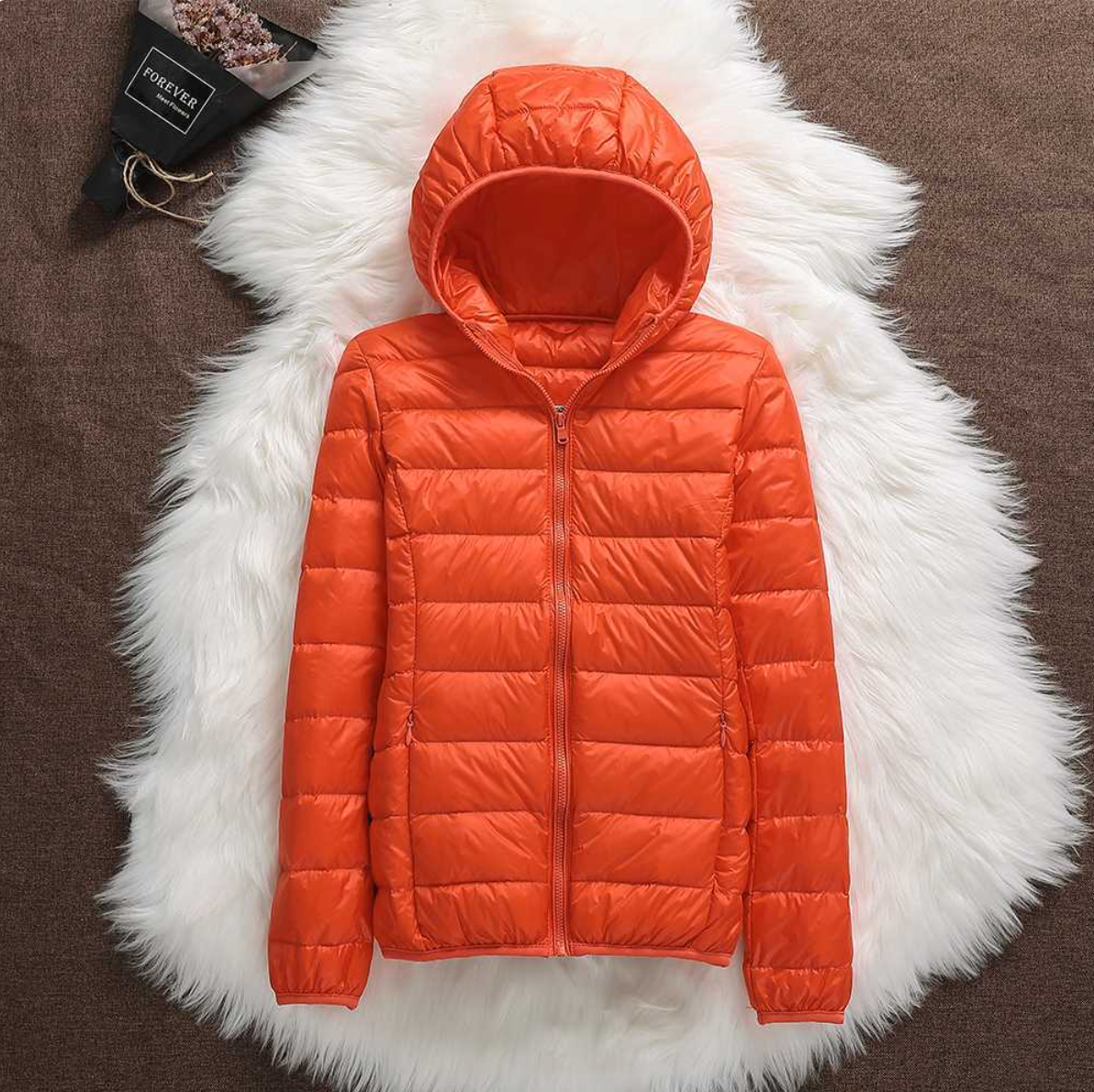 Giacca piumino arancione con cappuccio su sfondo di pelliccia bianca, moda invernale, abbigliamento caldo e leggero, stile casual.