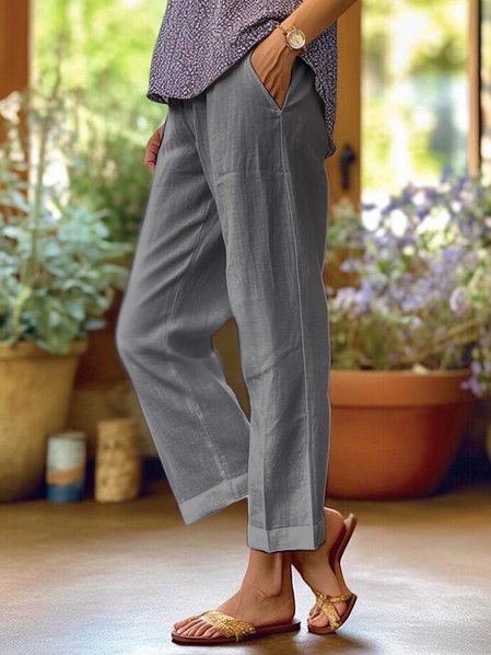 Pantaloni grigi in lino, donna in sandali dorati, ambiente esterno con piante in vaso, moda estiva casual, comfort e stile.