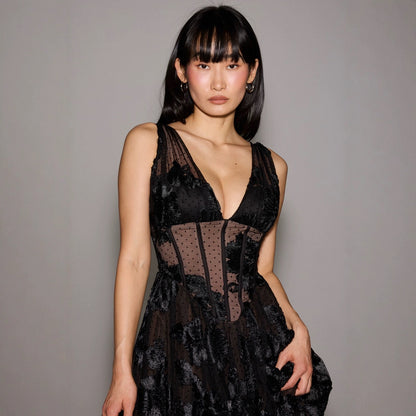 Donna in abito nero elegante con dettagli in pizzo, posa su sfondo grigio. Moda femminile, abbigliamento da sera, stile sofisticato.