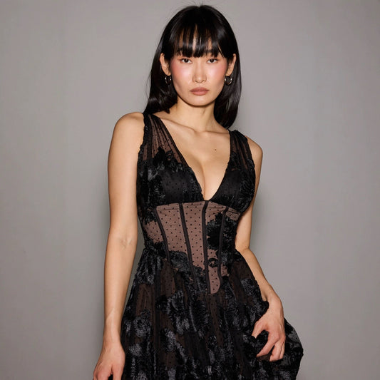 Donna in abito nero elegante con dettagli in pizzo, posa su sfondo grigio. Moda femminile, abbigliamento da sera, stile sofisticato.