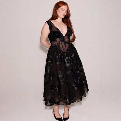 Donna con abito nero elegante in pizzo floreale, scollatura profonda, posa su sfondo neutro. Moda femminile, abbigliamento da sera, stile sofisticato.