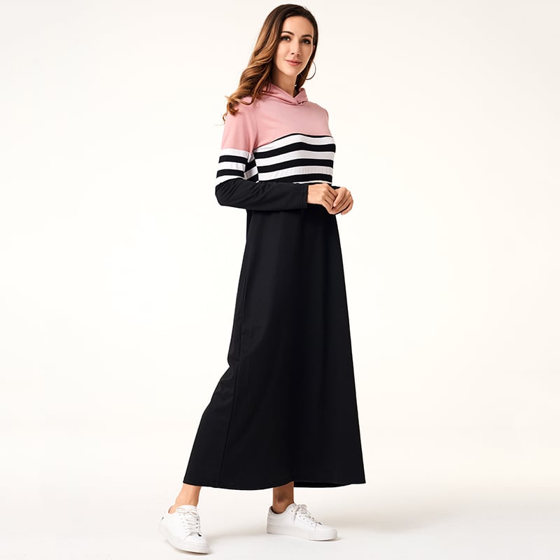 Donna in abito lungo casual a righe rosa e nere, con cappuccio, indossa scarpe da ginnastica bianche. Moda femminile, abbigliamento comodo.