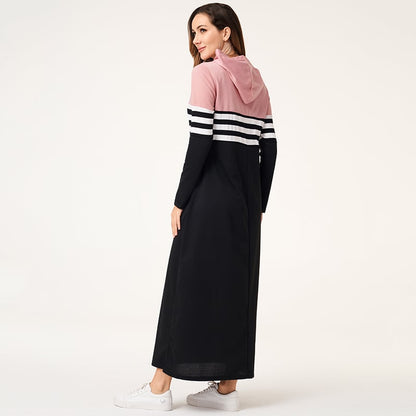 Donna in abito lungo sportivo nero e rosa con cappuccio, righe bianche, scarpe da ginnastica bianche. Moda casual femminile, abbigliamento comodo.