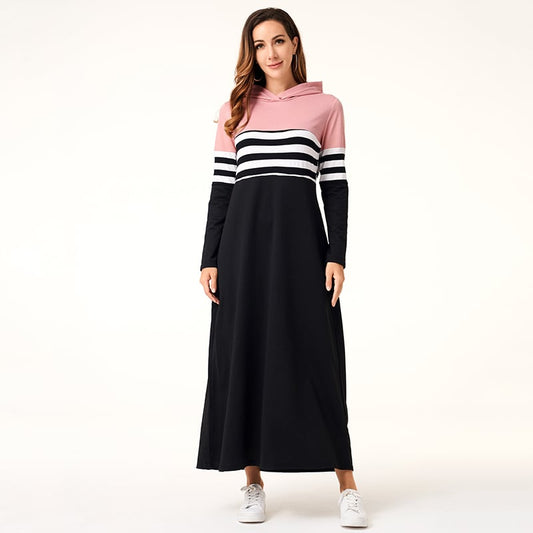 Donna in abito lungo casual a righe rosa, bianco e nero con cappuccio, indossa scarpe da ginnastica bianche. Moda femminile, abbigliamento casual.