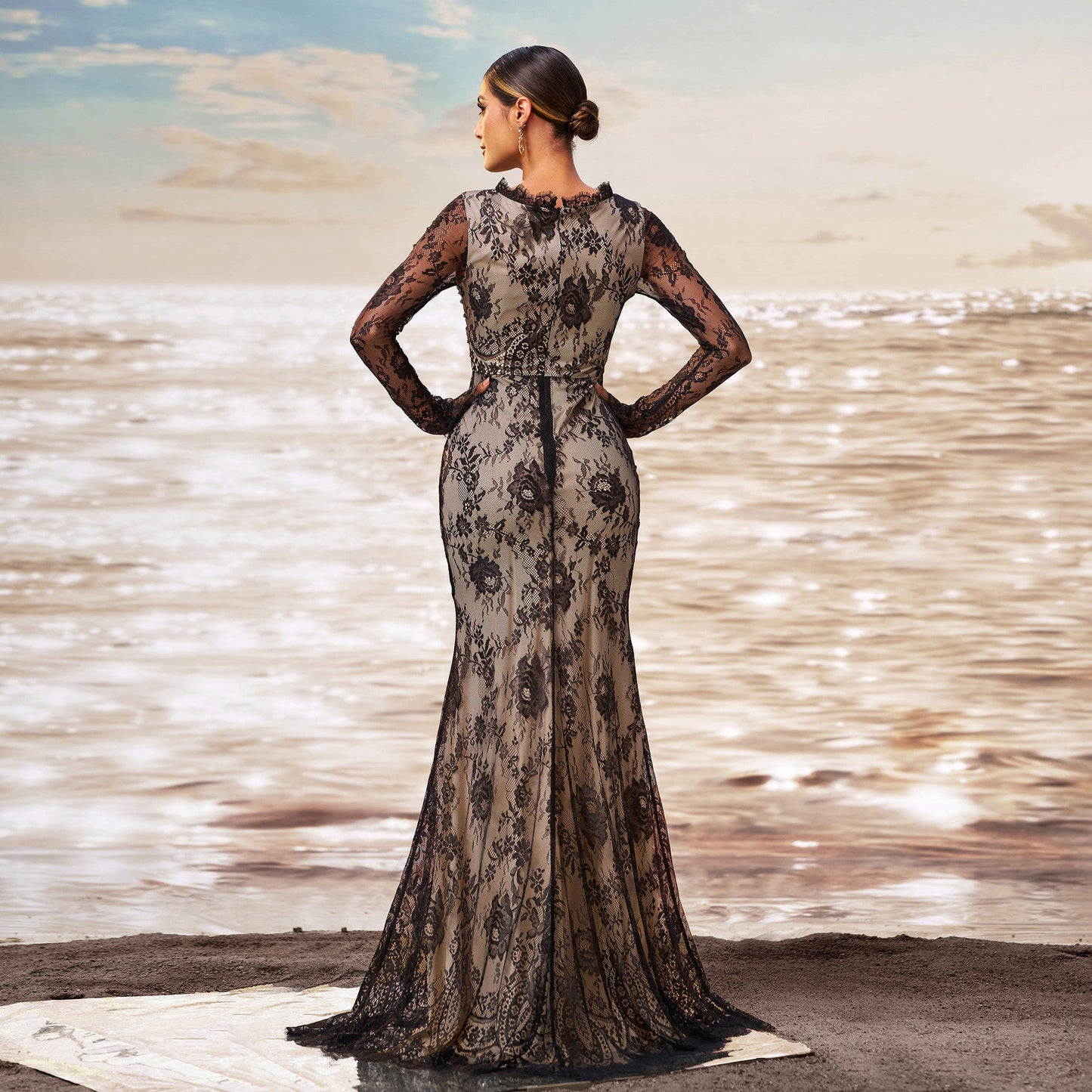 Donna in abito da sera lungo in pizzo nero, elegante e sofisticato, su spiaggia al tramonto. Moda femminile, abbigliamento da cerimonia, stile glamour.