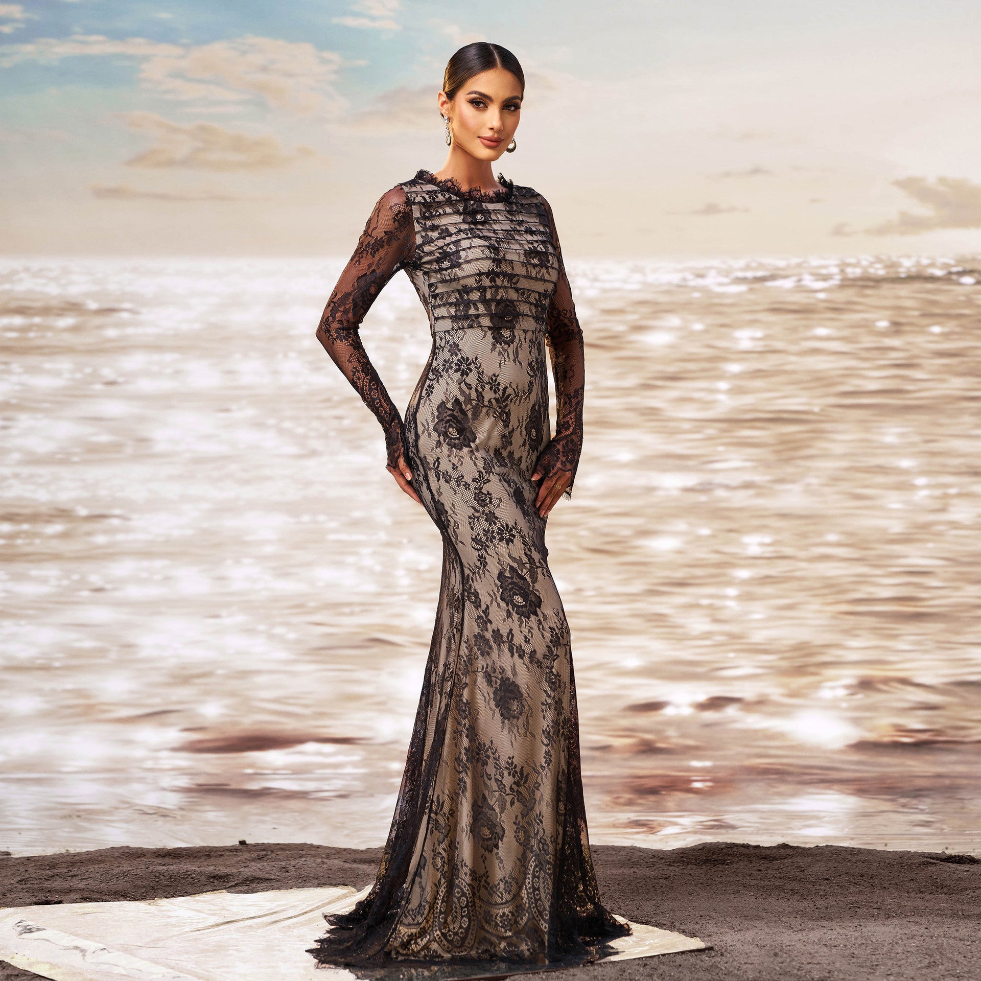 Donna in abito da sera lungo in pizzo nero, elegante e sofisticato, su spiaggia al tramonto. Moda femminile, abbigliamento di lusso, stile glamour.