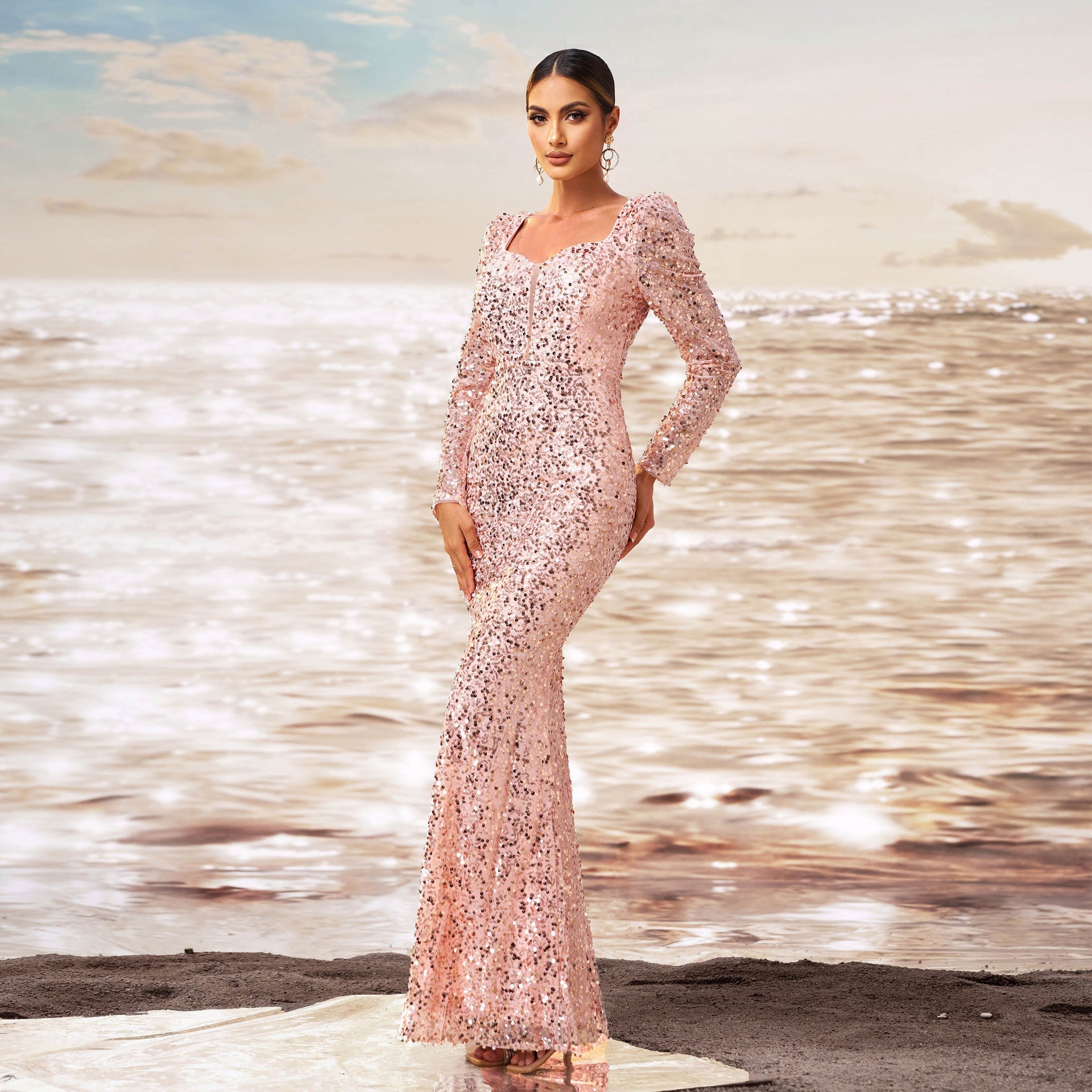 Donna in abito da sera rosa scintillante su spiaggia al tramonto, moda elegante, abito lungo con paillettes, sfondo mare e cielo nuvoloso.