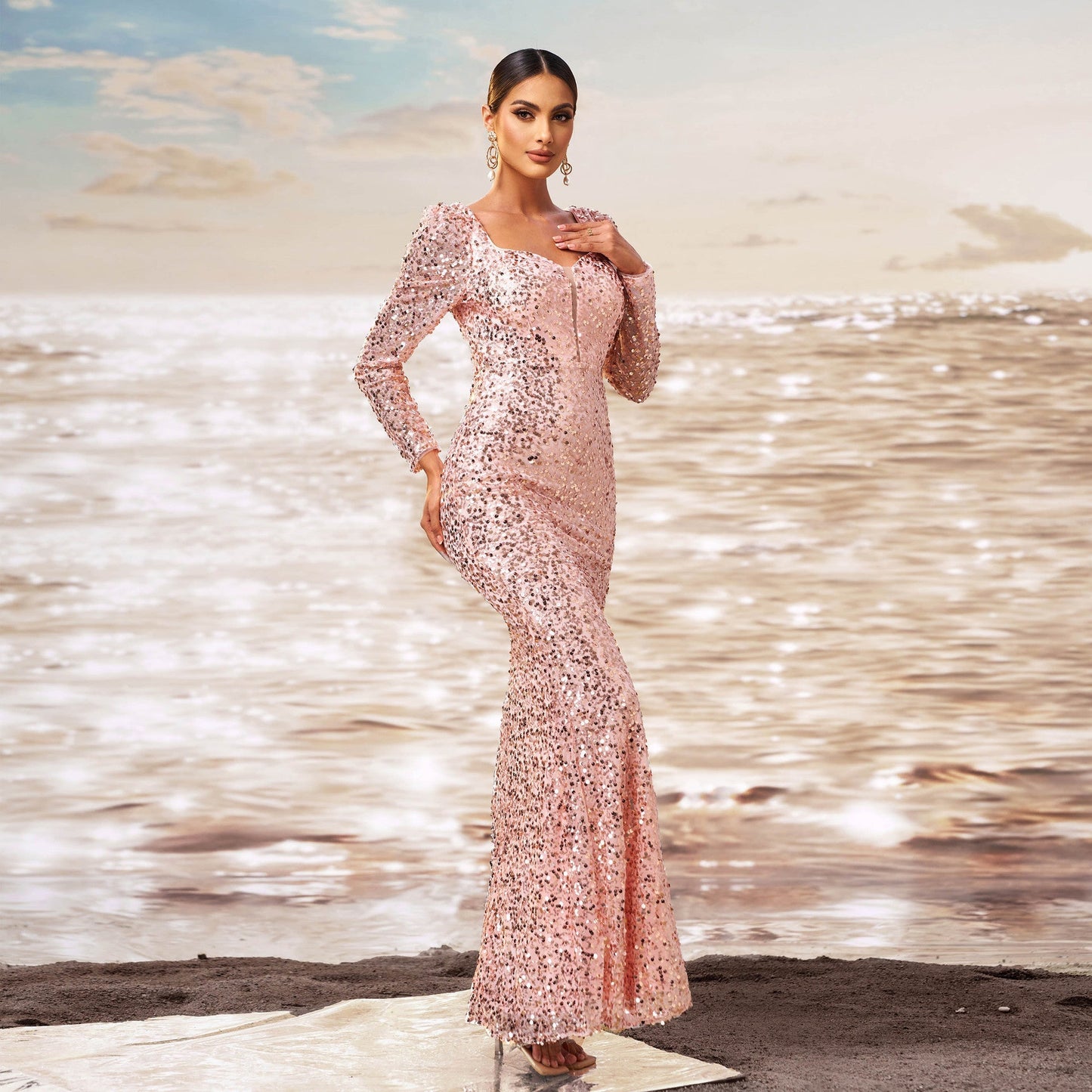 Donna in abito lungo rosa scintillante su spiaggia al tramonto, moda elegante, abbigliamento da sera, stile glamour, mare sullo sfondo.