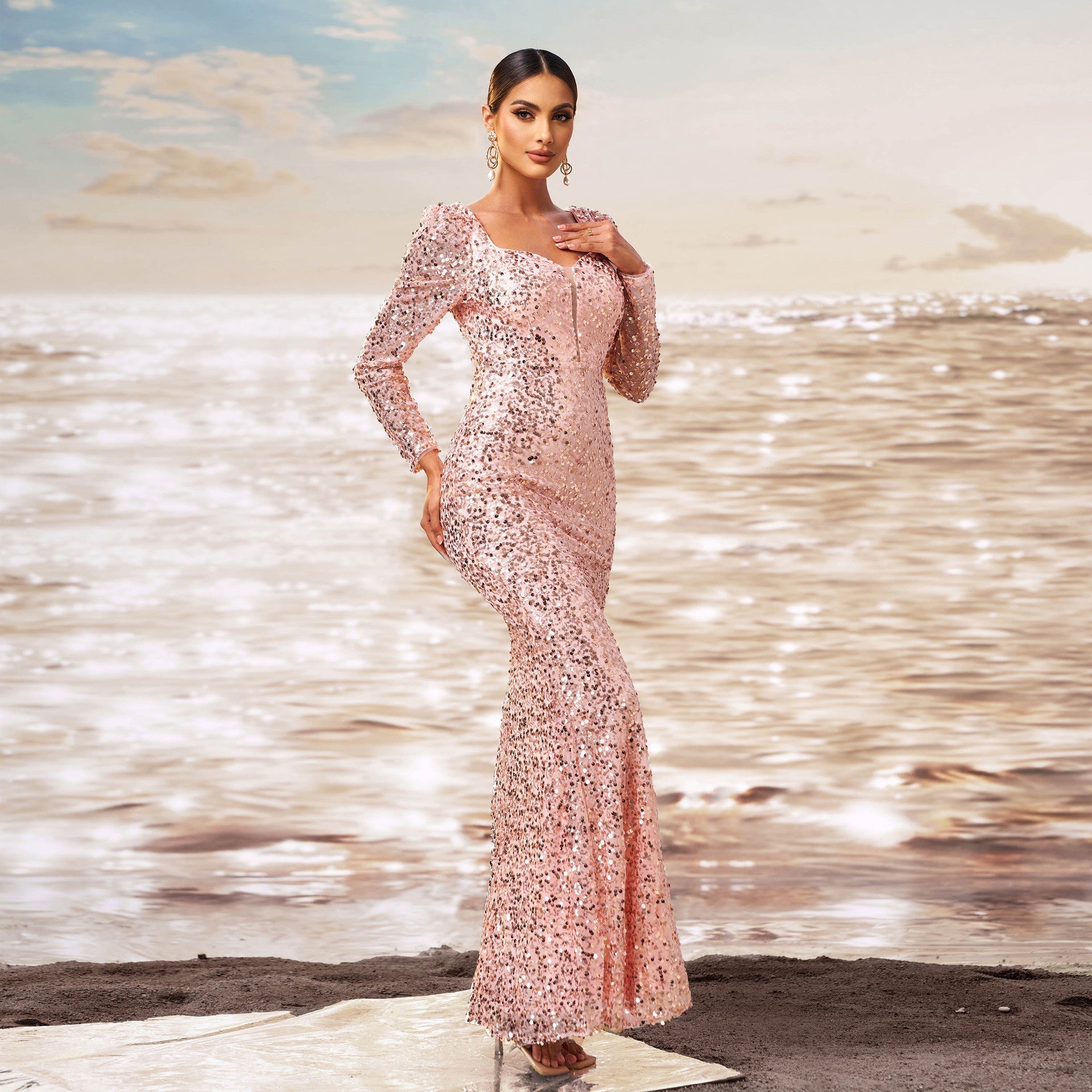 Donna in abito lungo rosa scintillante su spiaggia al tramonto, moda elegante, abbigliamento da sera, stile glamour, mare sullo sfondo.