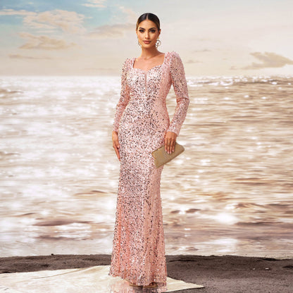 Donna in abito da sera rosa scintillante, con pochette dorata, in piedi su una spiaggia al tramonto. Eleganza, moda, abito da cerimonia.