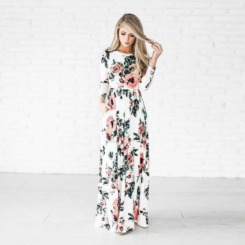 Donna in abito lungo floreale bianco e rosa, posa elegante su sfondo bianco. Moda femminile, abbigliamento estivo, tendenze 2023.