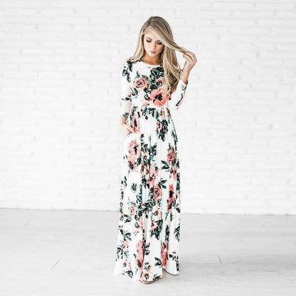 Donna in abito lungo floreale bianco e rosa, posa elegante su sfondo bianco. Moda femminile, abbigliamento estivo, tendenze 2023.