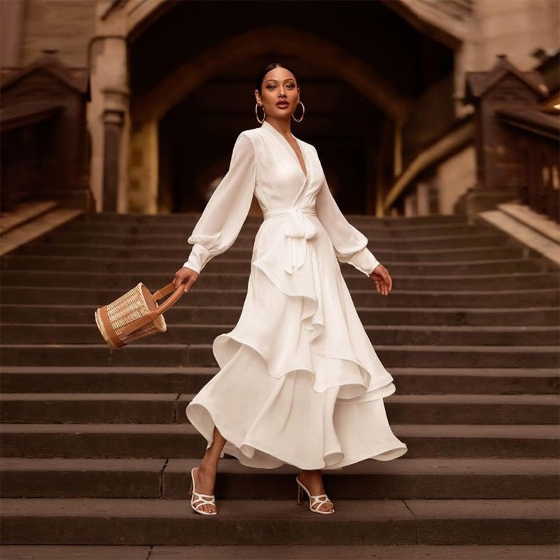 Donna elegante in abito bianco a balze su scala storica, con borsa di paglia e sandali bianchi. Moda femminile, stile sofisticato, abbigliamento estivo.