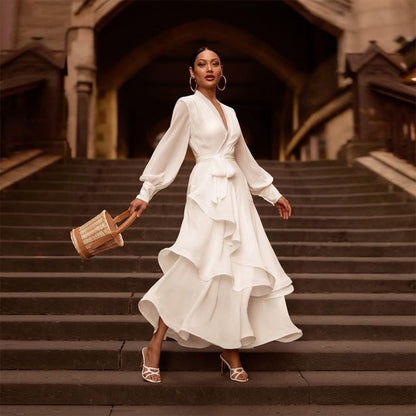 Donna elegante in abito bianco a balze su scala storica, con borsa di paglia e sandali bianchi. Moda femminile, stile sofisticato, abbigliamento estivo.