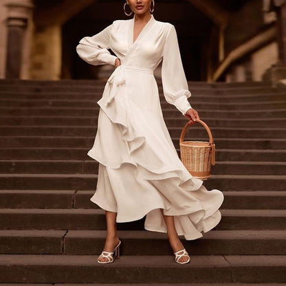 Donna in abito bianco elegante con volant, sandali bianchi e borsa di paglia su gradini. Moda femminile, stile estivo, abbigliamento chic.