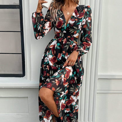 Abito lungo floreale nero con scollo a V e maniche lunghe, indossato da una donna davanti a una finestra. Moda autunnale elegante e femminile.