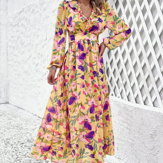 Abito lungo floreale giallo con motivi rosa e viola, maniche lunghe, scollo a V, sfondo bianco, moda estiva femminile elegante.