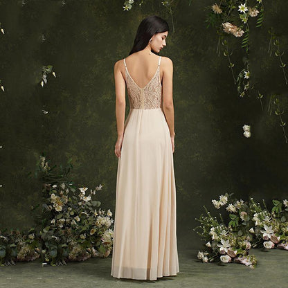 Donna in abito da sera lungo color crema con schiena in pizzo, circondata da fiori e vegetazione. Elegante abbigliamento da cerimonia.