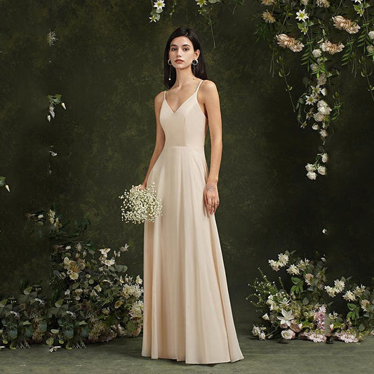 Donna in abito da sera beige lungo, con bouquet di fiori bianchi, circondata da decorazioni floreali verdi e bianche. Eleganza e moda femminile.