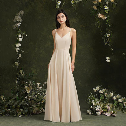 Donna in abito da sera lungo color crema, circondata da fiori e vegetazione. Elegante vestito da cerimonia, moda femminile, stile sofisticato.