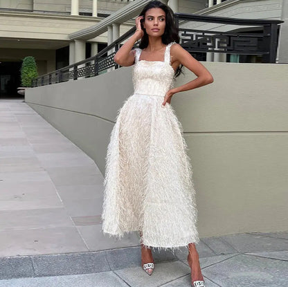 Donna in abito bianco elegante con frange, posa all'aperto. Moda femminile, abbigliamento da sera, stile glamour. Scarpe con tacco decorate.