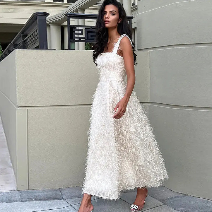 Donna in abito bianco elegante con dettagli piumati, posa all'aperto su marciapiede. Moda femminile, abbigliamento da sera, stile sofisticato.