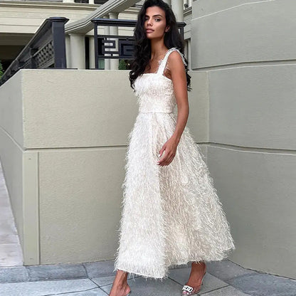 Donna in abito bianco elegante con dettagli piumati, posa all'aperto su marciapiede. Moda femminile, abbigliamento da sera, stile sofisticato.