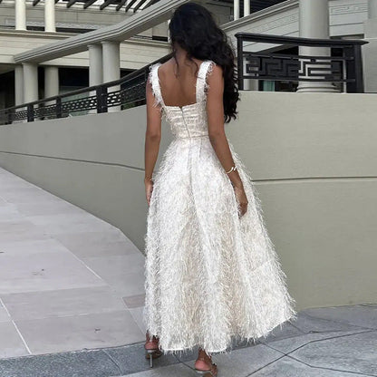 Donna in abito lungo bianco con frange, vista di spalle, su passerella moderna. Moda elegante, abbigliamento da sera, stile sofisticato.