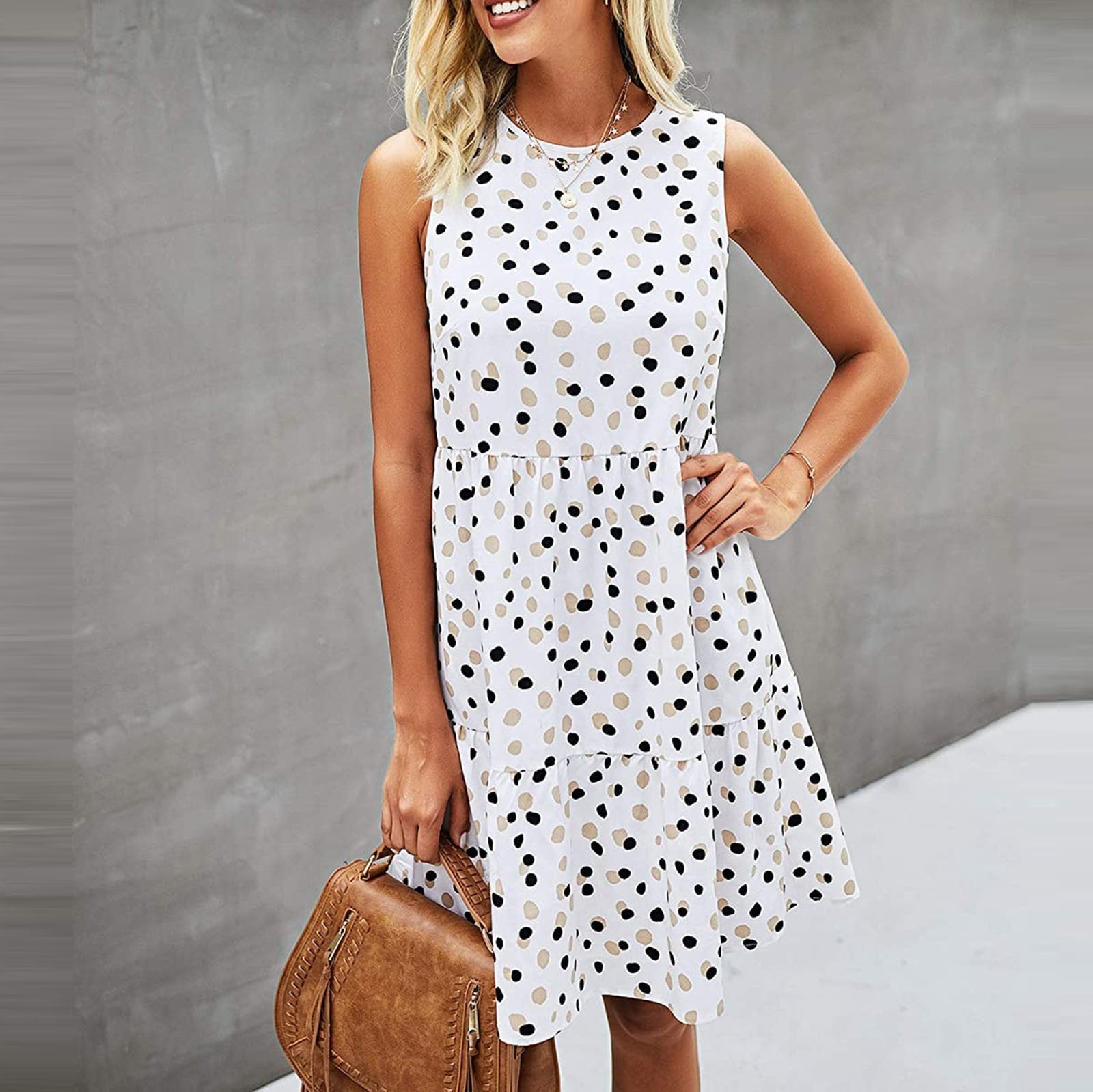 Abito estivo a pois bianchi e neri, senza maniche, indossato da una donna con borsa marrone. Moda casual femminile, look estivo elegante.