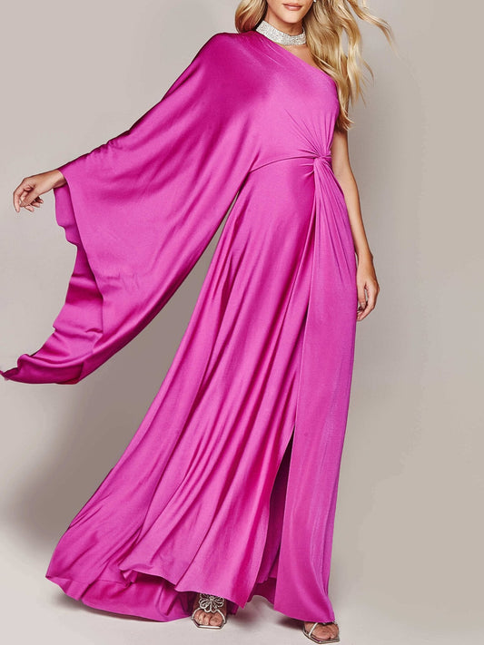 Abito lungo elegante fucsia con manica a mantella, tessuto fluente, indossato da modella bionda. Perfetto per eventi serali e cerimonie.