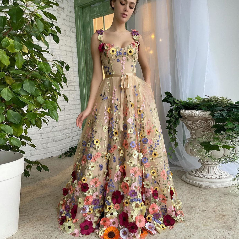 Abito da sera floreale, donna in vestito lungo con fiori colorati, ambientazione elegante con piante verdi e decorazioni classiche.